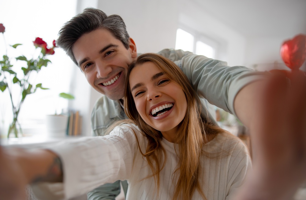 Smiling couple taking a selfie together indoors, showcasing healthy and confident smiles – Santa Paula Dentist
